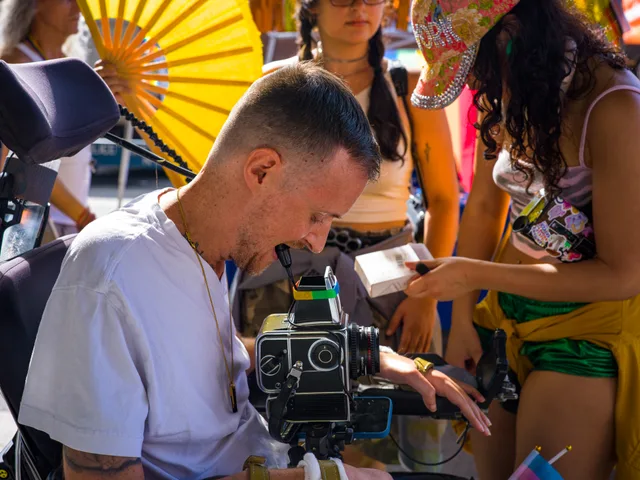 Close view of people adjusting camera equipment mounted before a wheelchair user.