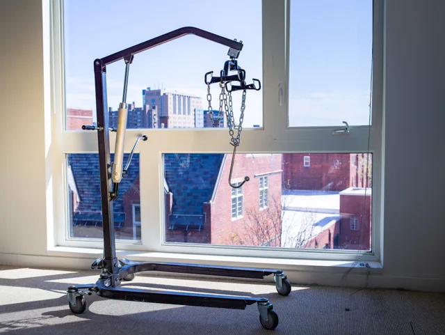 An empty ceiling lift stands before a row of city windows.