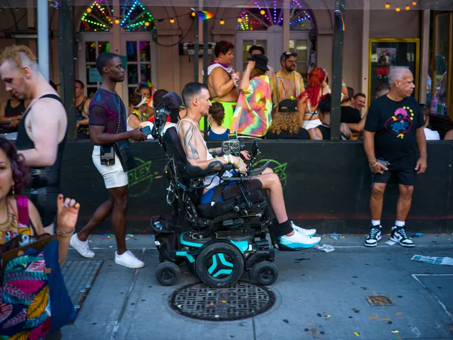 A wheelchair user sits among a crowd outside an ornate building.