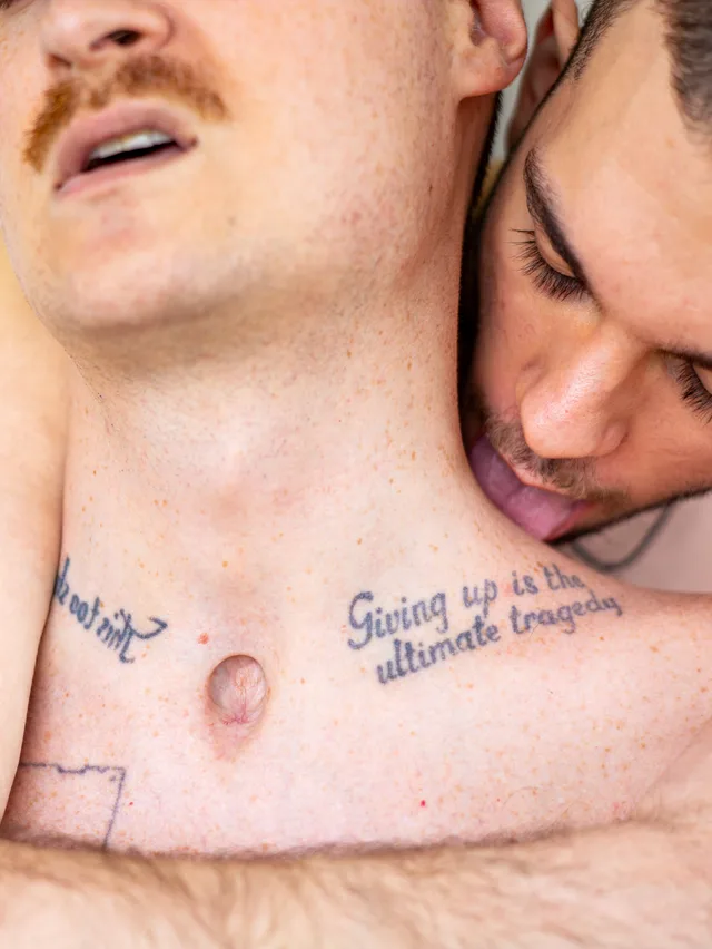 Close-up of two faces against a bare chest tattooed with the words 'Giving up is the ultimate tragedy.'