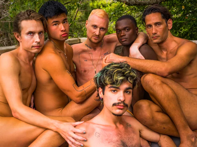 Six shirtless and nude people press together for a close outdoor group portrait.