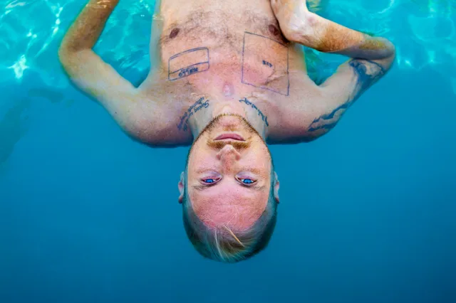 Upside-down view of a shirtless person floating in bright blue water.