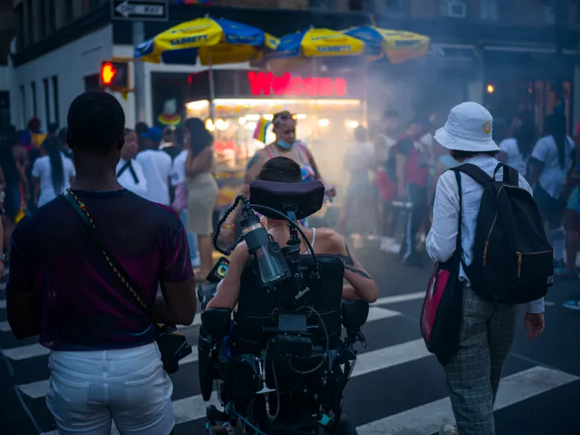 A wheelchair user moves through smoke and a crowded city street.