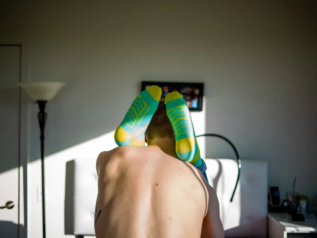 A nude person bends forward with bright patterned fabric draped over their head.