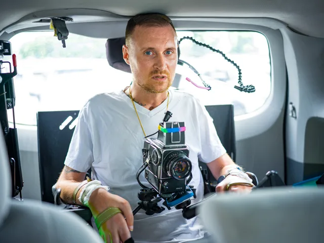 A wheelchair user wearing a chest-mounted camera sits inside a vehicle.