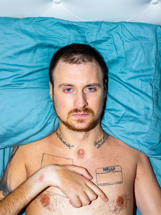 A shirtless person lies on a turquoise sheet, looking directly at the camera with one hand on their chest.